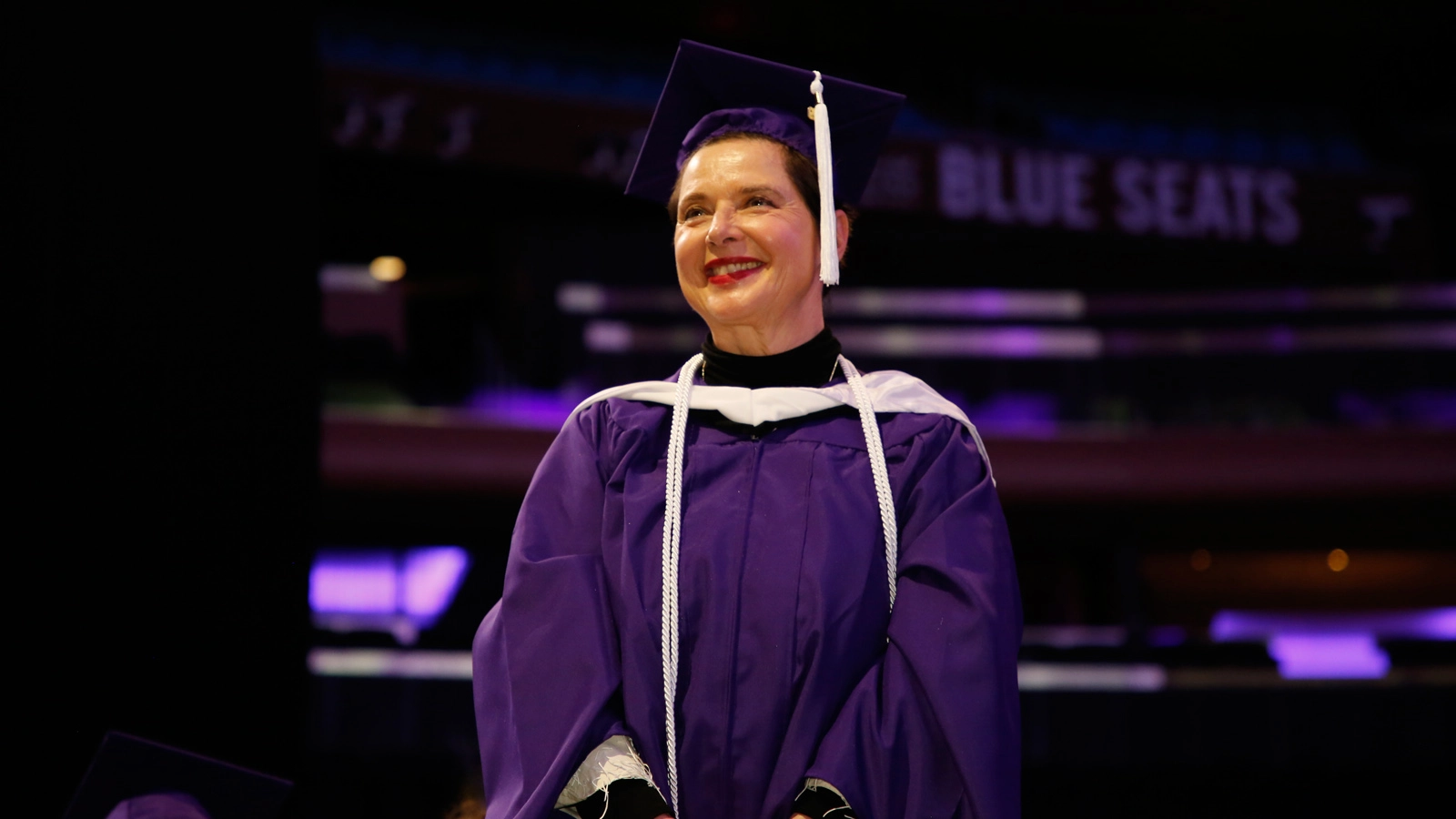 An ABC student in a purple cap and gown smiles at her graduation