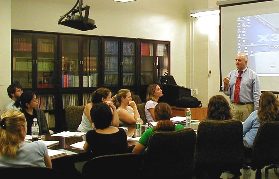 Students sit around a table in a lecture roo, listening to a presentation by an ABC faculty member